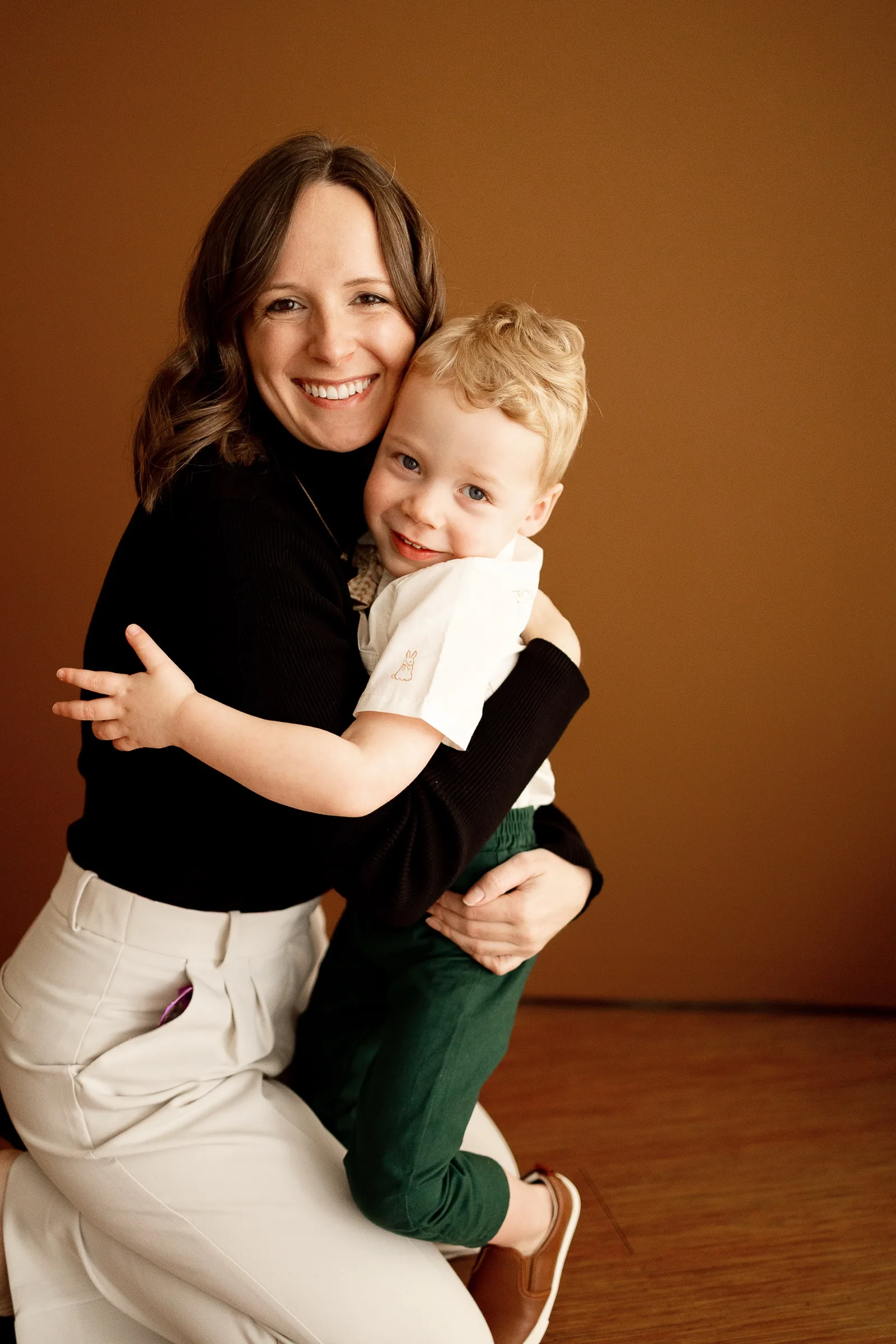 Emily hugging her son in a warm-toned studio, both laughing.